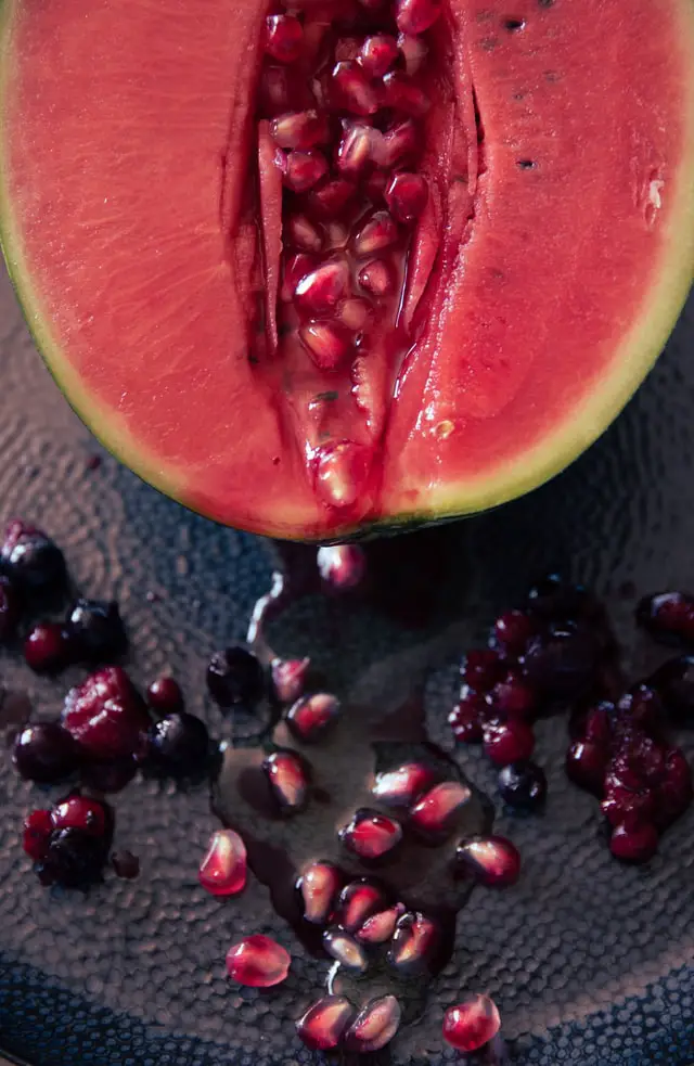 Photo of a juicy, pink watermelon half drenched in red pomegranate seeds and blueberries. erotic energy has political potential!